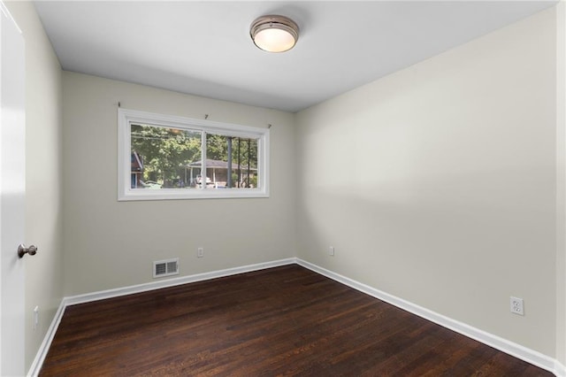 spare room featuring dark wood-type flooring, visible vents, and baseboards