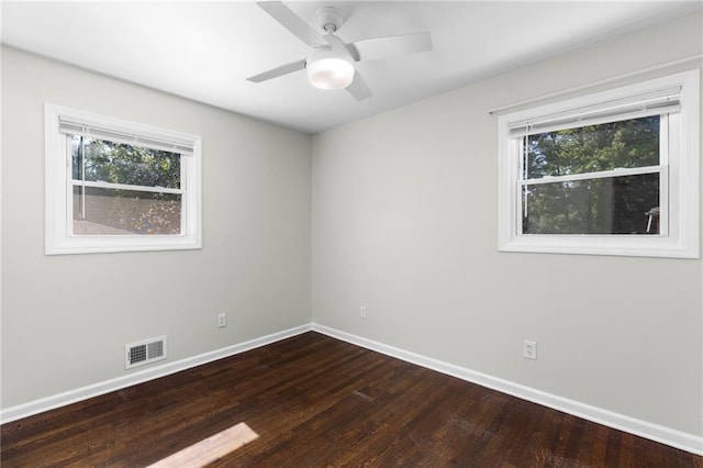 empty room featuring dark wood-type flooring, a wealth of natural light, visible vents, and baseboards