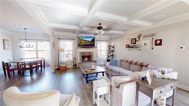 living area with a stone fireplace, ceiling fan with notable chandelier, coffered ceiling, wood finished floors, and beamed ceiling