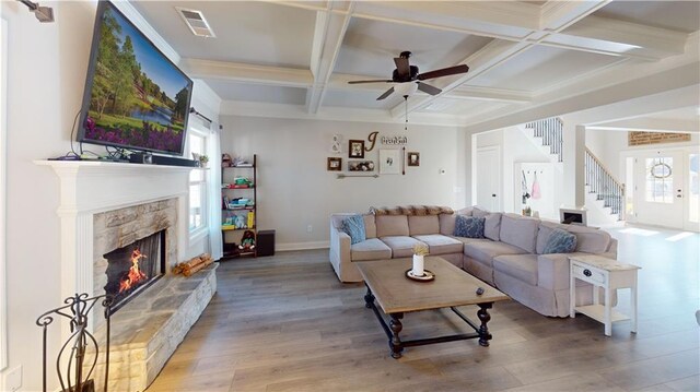 living room featuring a fireplace, coffered ceiling, visible vents, stairs, and light wood-type flooring