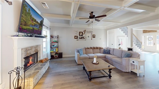 living room featuring a stone fireplace, hardwood / wood-style floors, coffered ceiling, ceiling fan, and beam ceiling