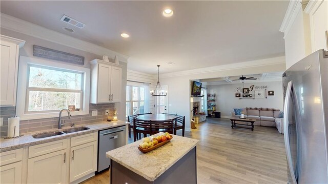 kitchen featuring visible vents, appliances with stainless steel finishes, open floor plan, crown molding, and a sink