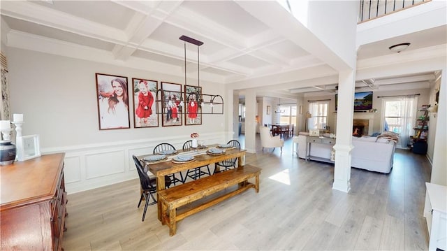 dining room with a warm lit fireplace, a wainscoted wall, coffered ceiling, light wood finished floors, and beamed ceiling