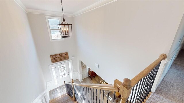 staircase featuring visible vents, a high ceiling, ornamental molding, and a chandelier