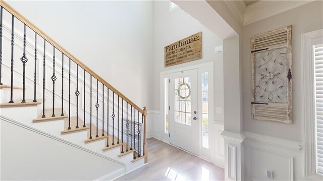 foyer entrance with wainscoting, wood finished floors, stairs, crown molding, and a decorative wall