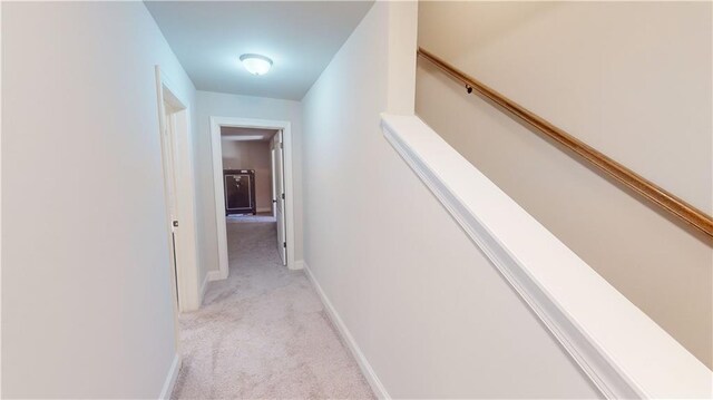 hall featuring light colored carpet, baseboards, and stairs