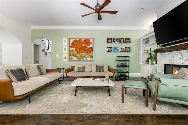 living area with ceiling fan, wood finished floors, crown molding, stairway, and a fireplace