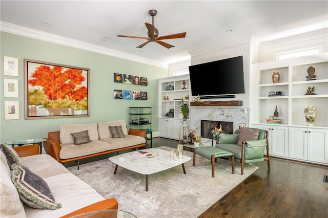living room with crown molding, ceiling fan, wood finished floors, a fireplace, and built in features