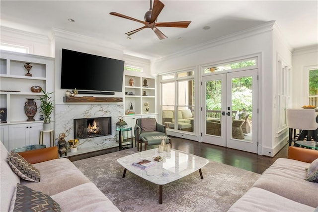 living room with ornamental molding, a high end fireplace, ceiling fan, french doors, and wood finished floors