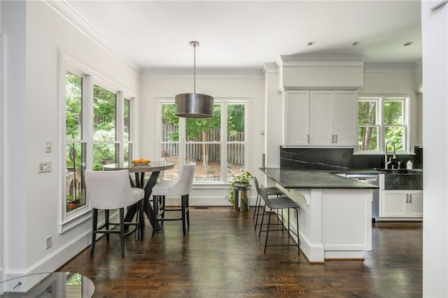kitchen with dark countertops, plenty of natural light, dishwasher, a breakfast bar, and crown molding