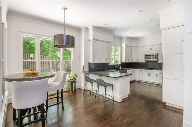 kitchen with stainless steel microwave, a peninsula, decorative backsplash, dark countertops, and a breakfast bar area