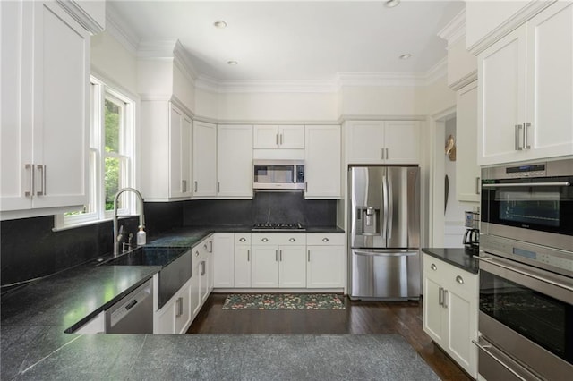kitchen with stainless steel appliances, dark countertops, a sink, tasteful backsplash, and white cabinetry