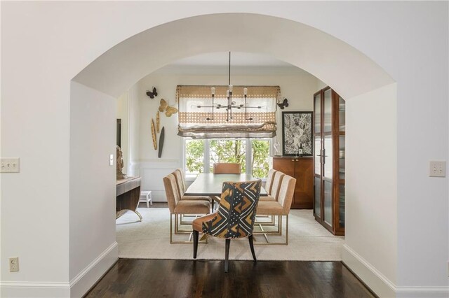 dining room featuring arched walkways, wood finished floors, baseboards, and a chandelier