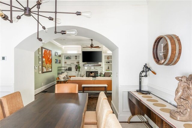 dining room with a ceiling fan, a warm lit fireplace, arched walkways, ornamental molding, and built in features