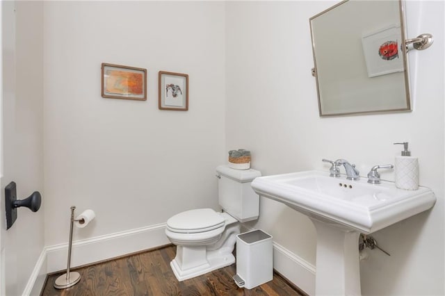 half bath featuring baseboards, toilet, wood finished floors, and a sink
