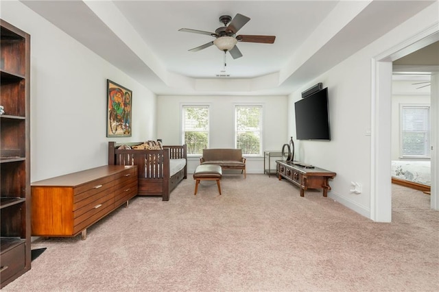 living area featuring light colored carpet, ceiling fan, a tray ceiling, and baseboards