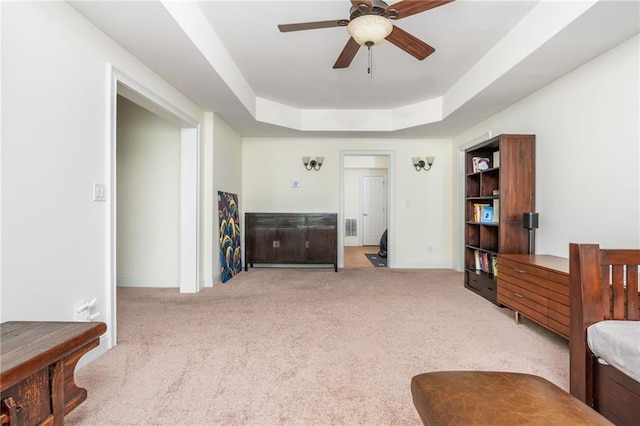 living area featuring light carpet, ceiling fan, baseboards, and a tray ceiling