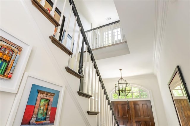 entryway with a chandelier, healthy amount of natural light, a high ceiling, stairway, and crown molding