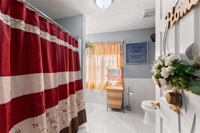 bathroom featuring toilet, a wainscoted wall, tile patterned flooring, a textured ceiling, and tile walls