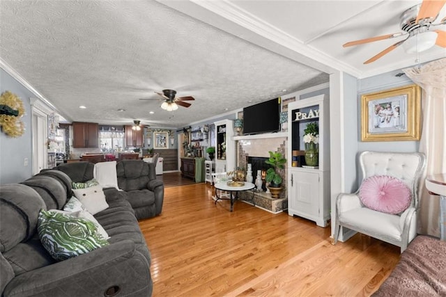 living room with a textured ceiling, ceiling fan, light wood finished floors, and crown molding