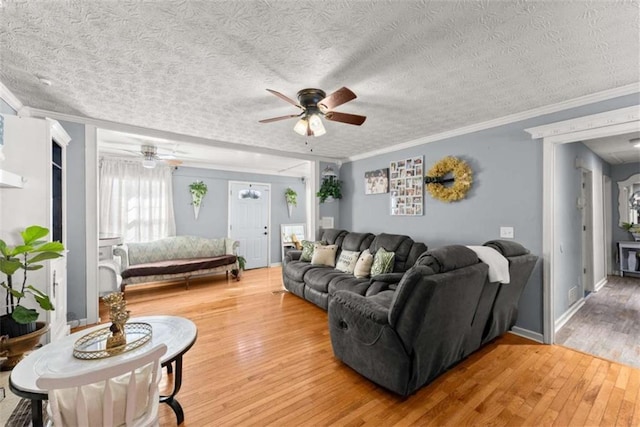 living area featuring ceiling fan, ornamental molding, a textured ceiling, and wood finished floors