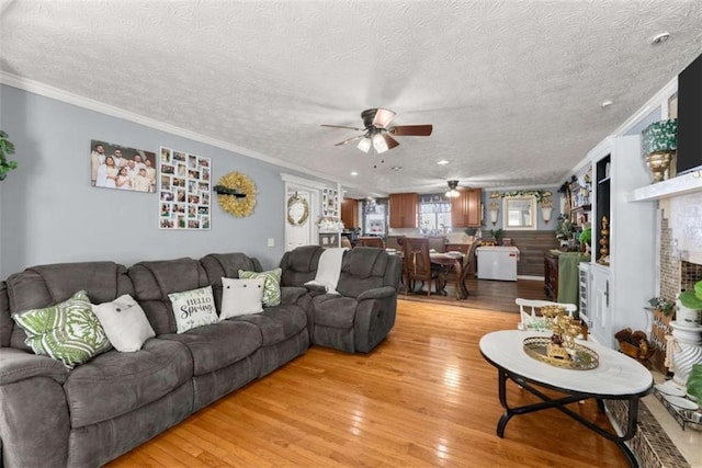 living area featuring light wood-style floors, ornamental molding, a textured ceiling, and a ceiling fan