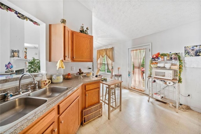 kitchen featuring a sink, white microwave, a textured ceiling, light countertops, and light floors