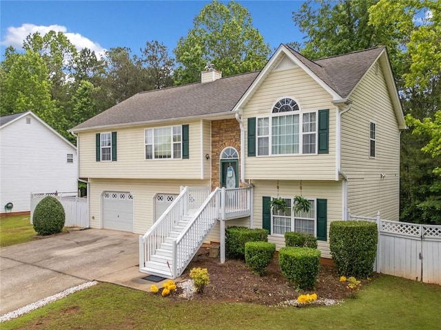 raised ranch with an attached garage, a chimney, driveway, and a shingled roof