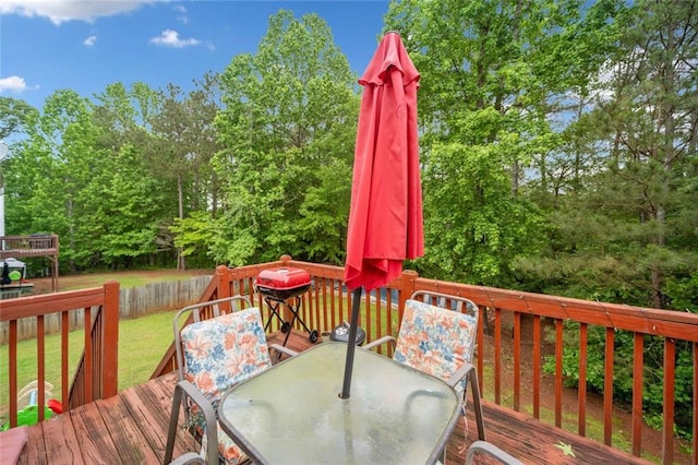 deck with outdoor dining area, a yard, and view of wooded area