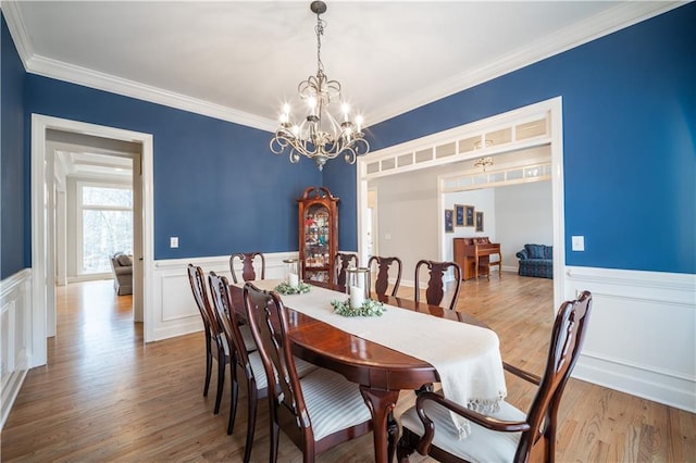 dining room with a chandelier, wainscoting, ornamental molding, wood finished floors, and a decorative wall