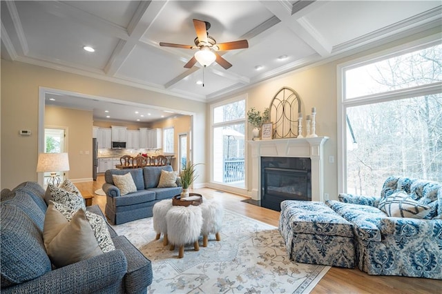 living area featuring coffered ceiling, light wood-type flooring, a ceiling fan, crown molding, and beam ceiling