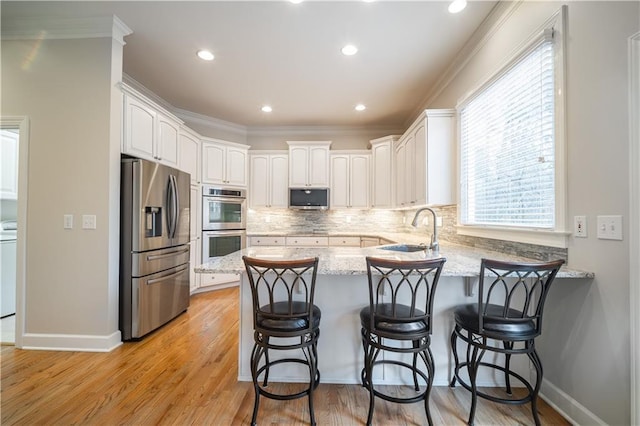 kitchen with appliances with stainless steel finishes, a peninsula, a sink, light stone countertops, and tasteful backsplash