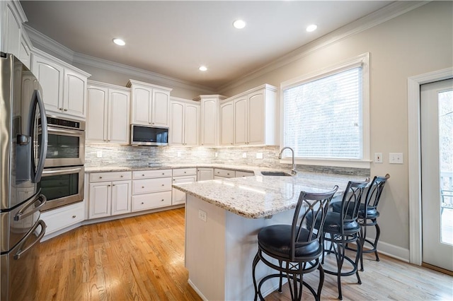kitchen with a sink, a peninsula, stainless steel appliances, a breakfast bar area, and light stone countertops