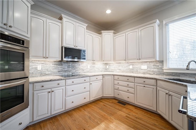 kitchen featuring a sink, appliances with stainless steel finishes, white cabinetry, decorative backsplash, and crown molding