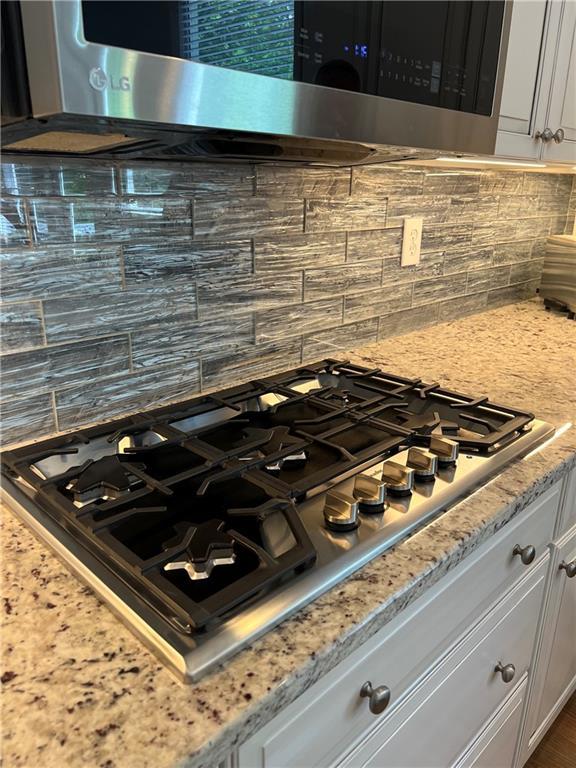 kitchen view of stainless steel appliances, decorative backsplash, white cabinetry, and light stone counters