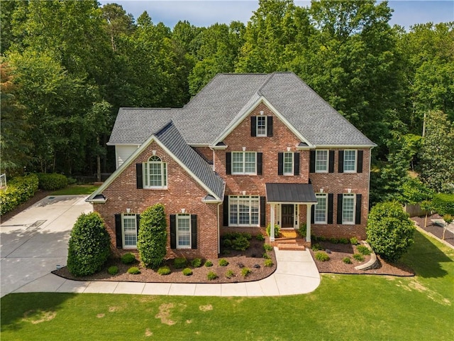 view of front of property with brick siding, a front yard, and a wooded view