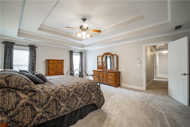 bedroom with a tray ceiling, light colored carpet, crown molding, attic access, and ceiling fan