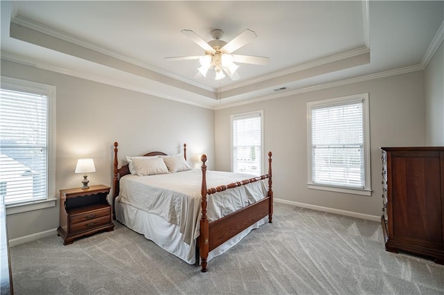 bedroom featuring a tray ceiling, crown molding, multiple windows, light colored carpet, and baseboards