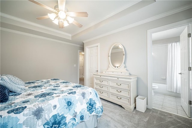 bedroom with a raised ceiling, light colored carpet, crown molding, ensuite bath, and ceiling fan