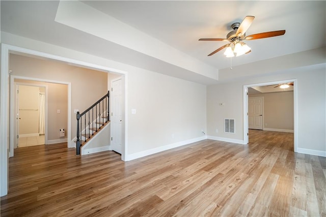 spare room with stairs, ceiling fan, light wood finished floors, and baseboards