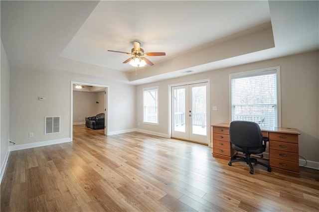 office featuring a tray ceiling, french doors, light wood finished floors, a ceiling fan, and healthy amount of natural light