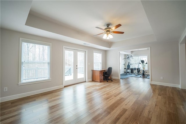 living area featuring a raised ceiling, french doors, a ceiling fan, light wood-style flooring, and an office area
