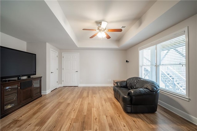 sitting room with baseboards, a ceiling fan, a raised ceiling, and light wood-type flooring