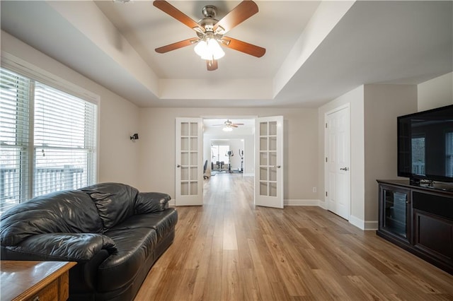 living room featuring french doors, a ceiling fan, a tray ceiling, and plenty of natural light