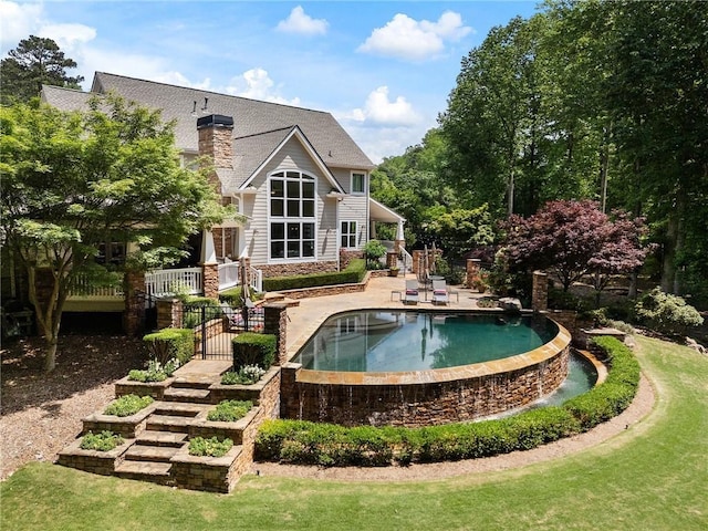 rear view of house with fence, stone siding, an outdoor pool, a patio, and a chimney