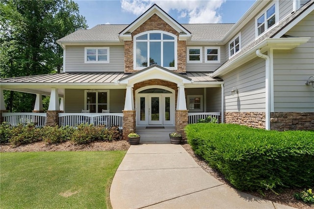 doorway to property featuring a standing seam roof, covered porch, a lawn, and stone siding