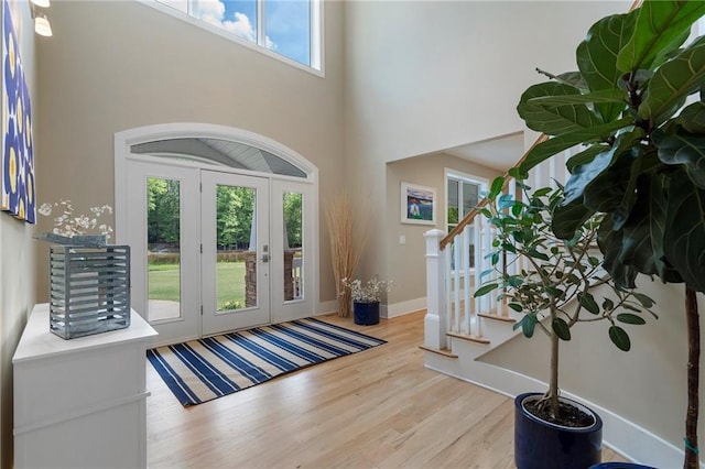 foyer entrance featuring french doors, wood finished floors, a towering ceiling, stairway, and baseboards