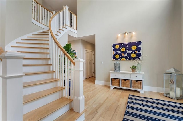 stairs with wood finished floors, baseboards, and a high ceiling