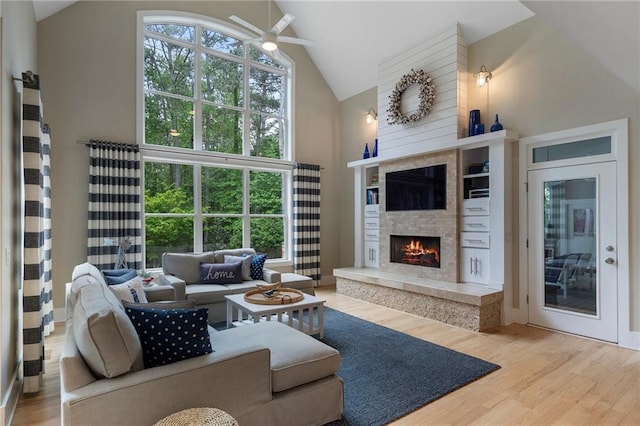 living area with a warm lit fireplace, high vaulted ceiling, ceiling fan, and wood finished floors