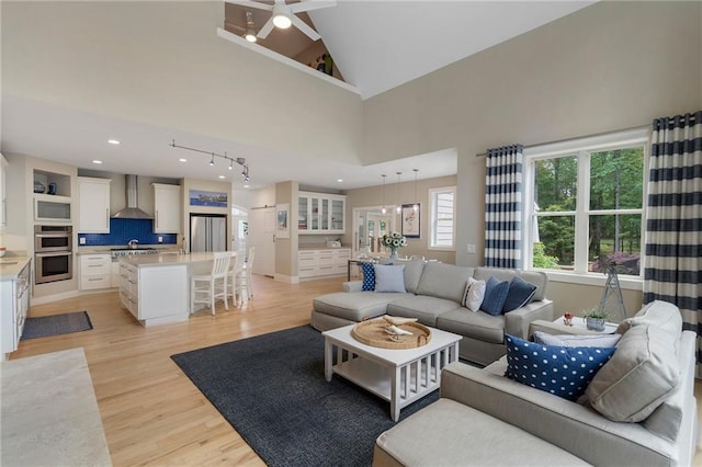 living room with ceiling fan, high vaulted ceiling, light wood-style flooring, recessed lighting, and baseboards
